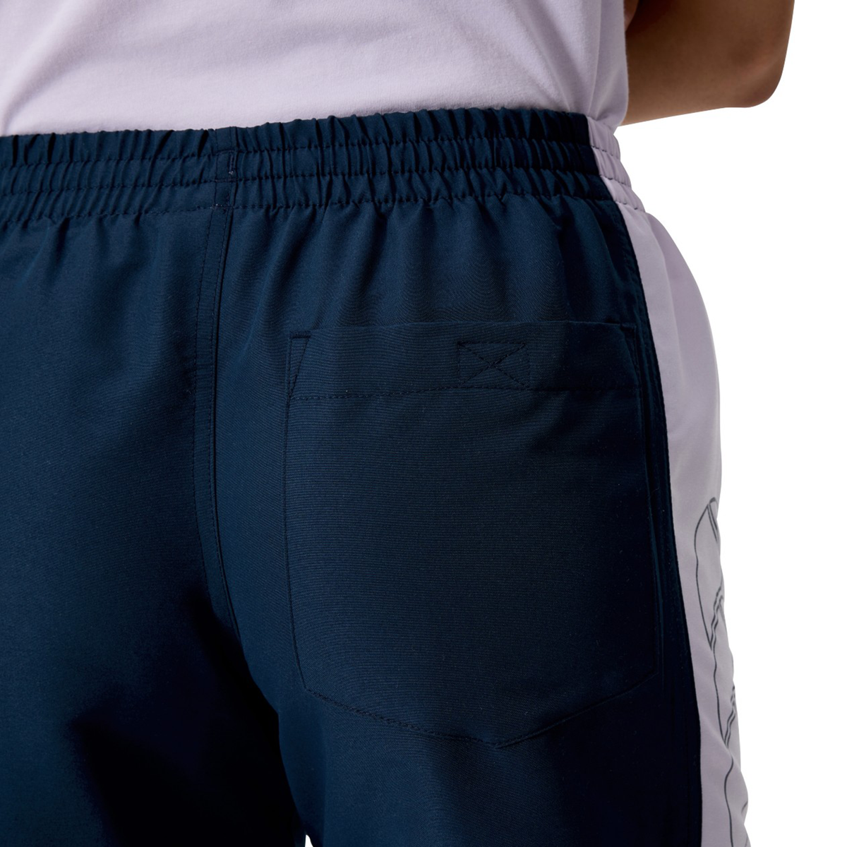 Close-up of a person wearing Canterbury Women's Fundamentals 5" Panel Tactic Shorts featuring a navy blue color, white side stripe, back pocket, and an elastic waistband.
