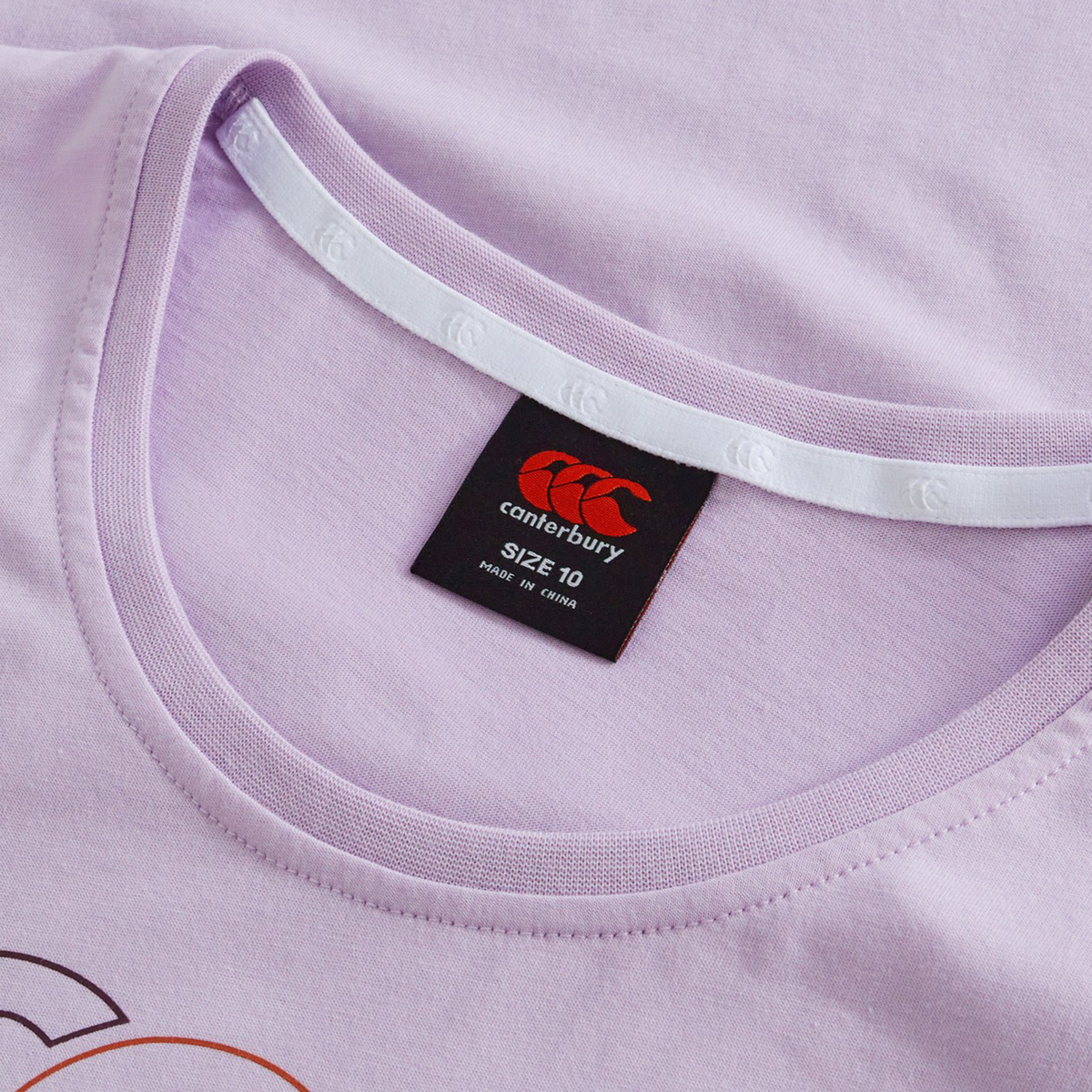 Close-up of the Women's Fundamentals CCC Logo T-Shirt by Canterbury, a light purple rugby tee for women, showing the collar, inner neck tape, and black size label with red logo and text indicating size 10 and made in China.