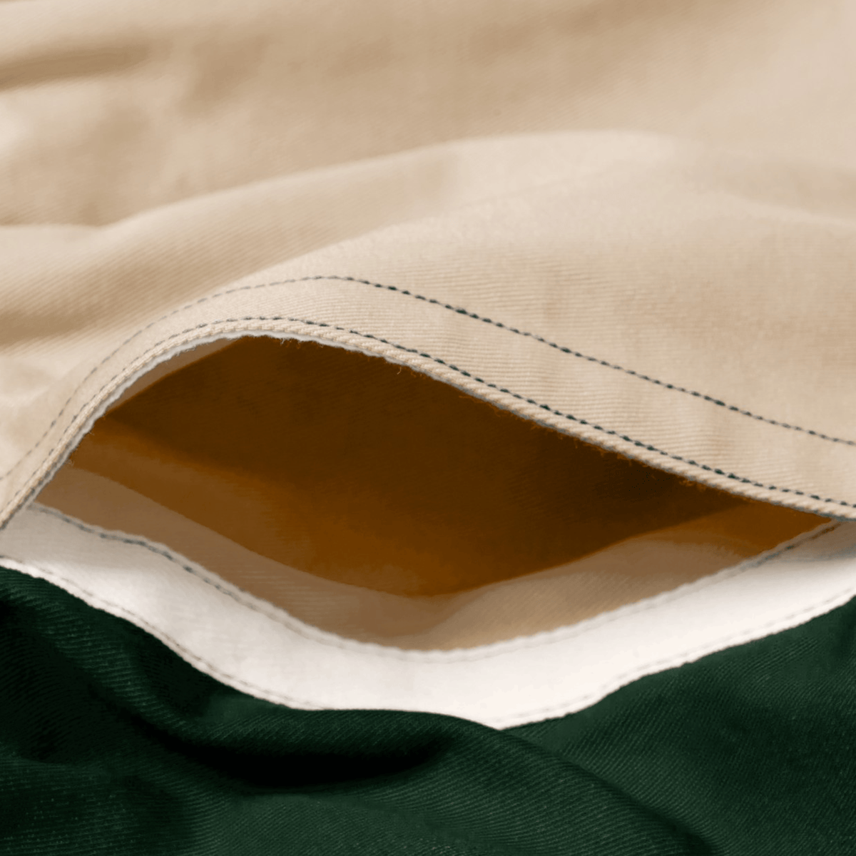 Close-up of Canterbury Fundamental Harlequin Drill Short by Canterbury, showing beige, white, and dark green layered fabric with visible stitching and a small opening, highlighting the brand's detailed craftsmanship.