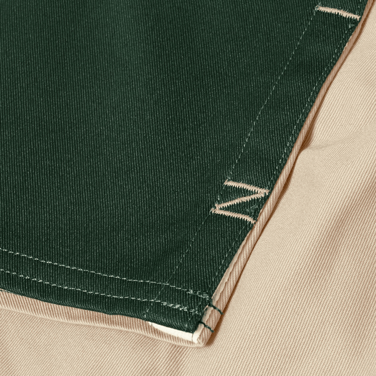 Close-up of green cotton fabric from Canterbury Fundamental Harlequin Drill Short by Canterbury, with visible stitching over beige fabric. Both fabrics feature a textured, diagonal weave pattern.
