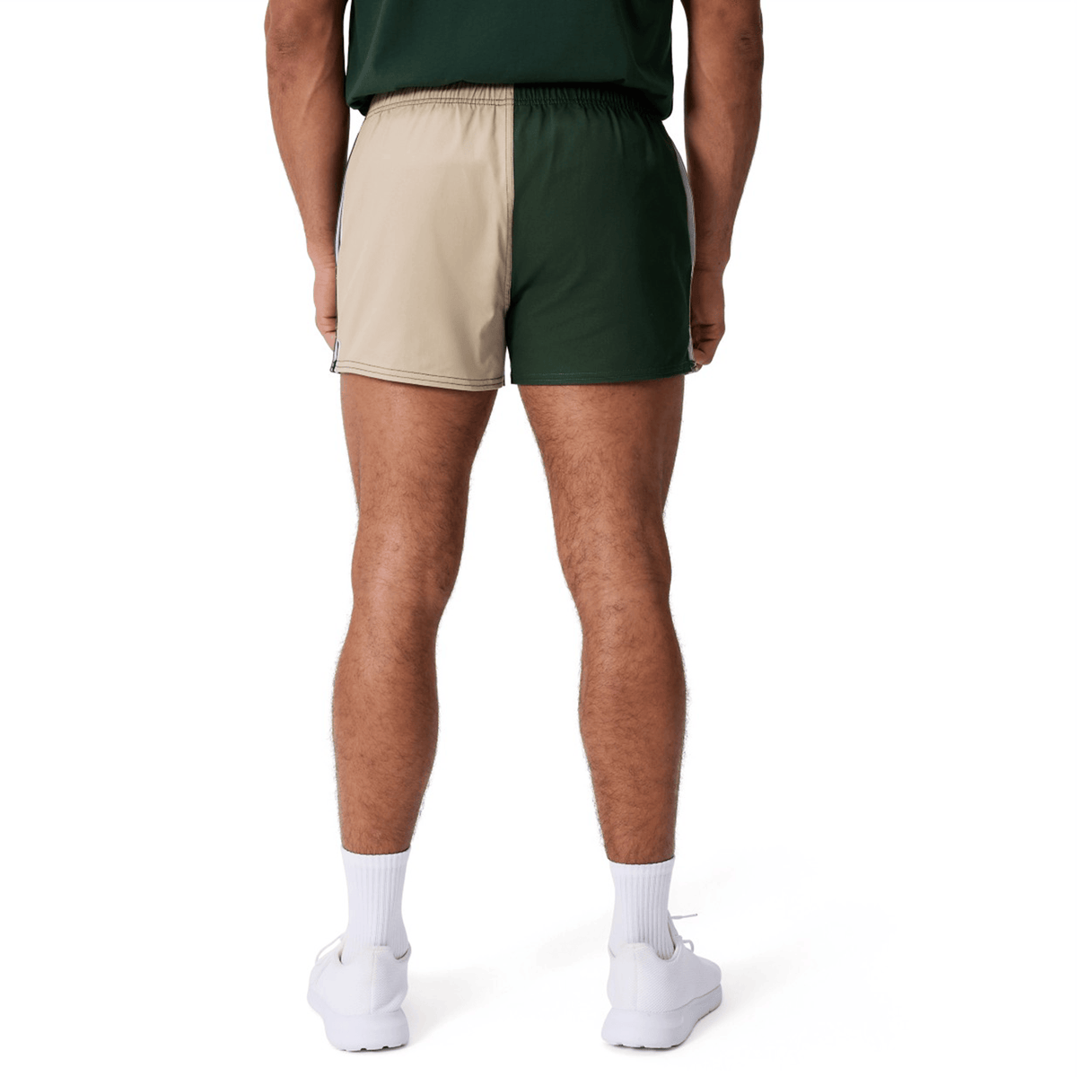 A person is shown from behind wearing Canterbury Fundamental Harlequin Drill Shorts by Canterbury—featuring tan and green panels—paired with white socks and white sneakers.