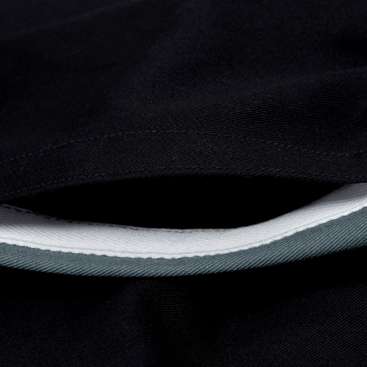 Close-up of Canterbury Fundamental Harlequin Drill Short by Canterbury in black, featuring a partially open seam that reveals its white and gray inner lining.