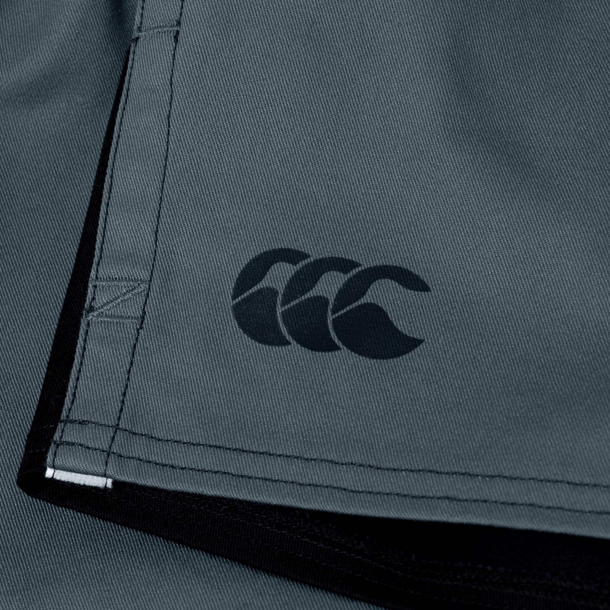 Close-up of grey Canterbury Fundamental Harlequin Drill Short fabric with visible stitching and a black Canterbury CCC logo.