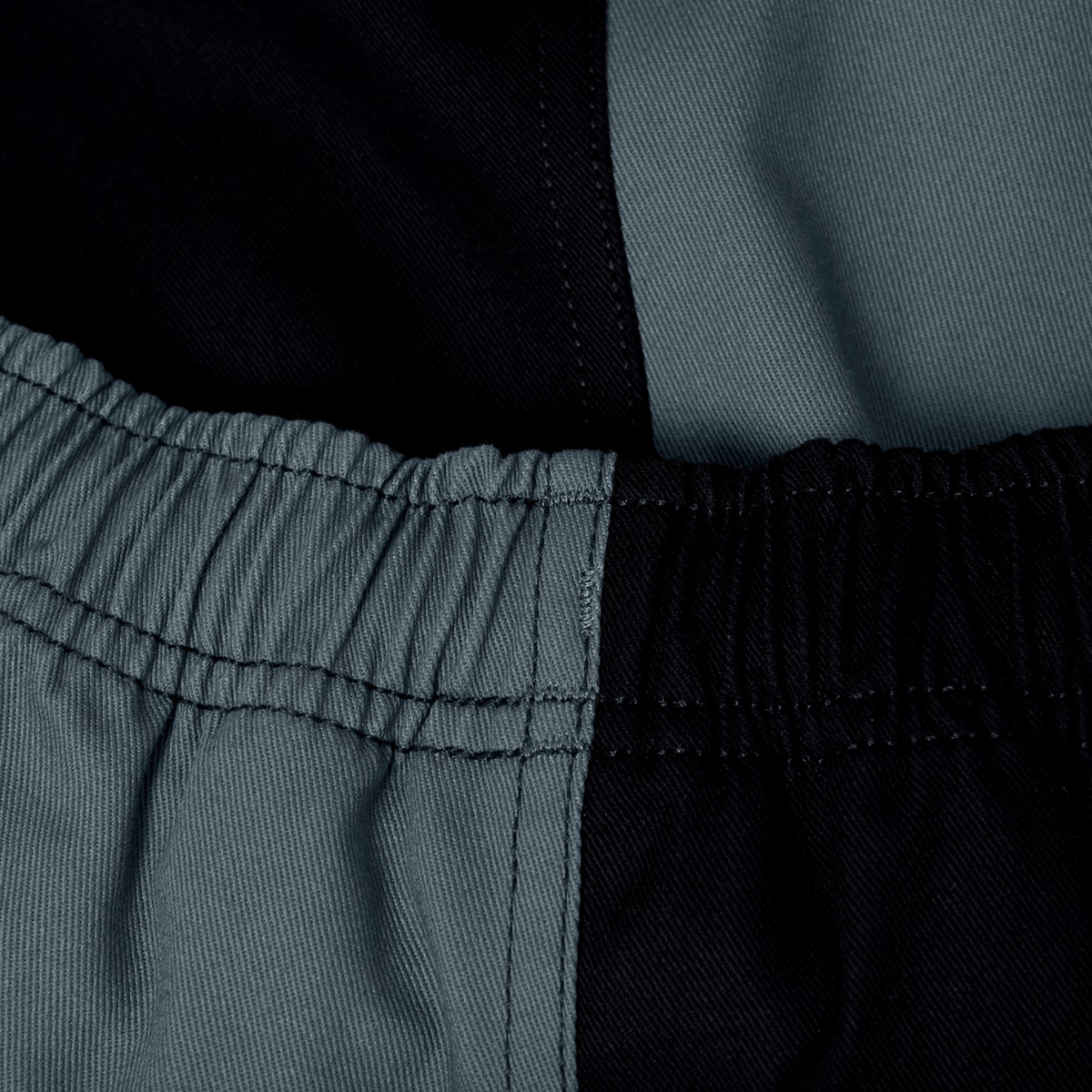 Close-up of Canterbury Fundamental Harlequin Drill Short by Canterbury, showcasing an elastic waistband and black and gray color-blocked fabric.
