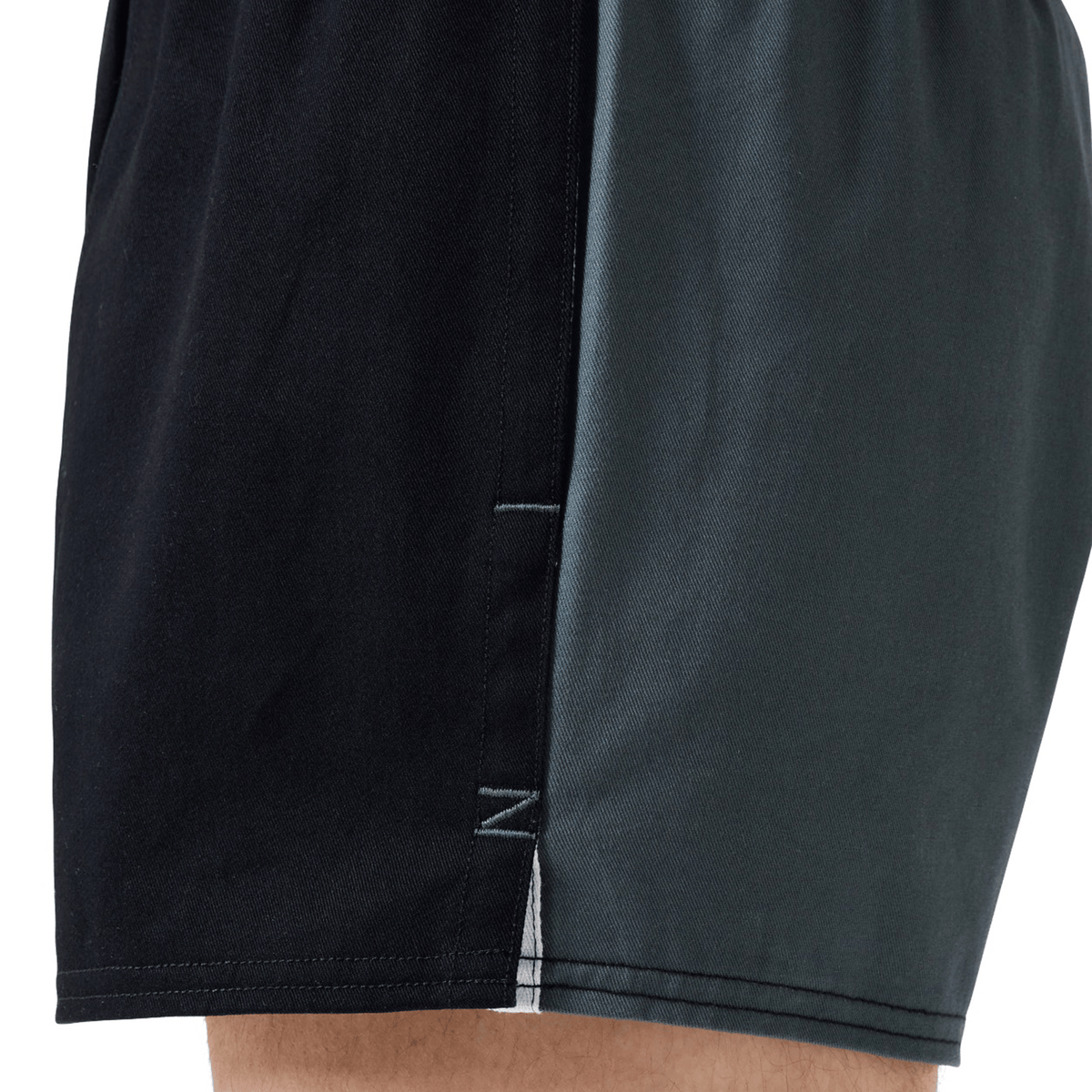 Close-up of a person wearing Canterbury Fundamental Harlequin Drill Shorts by Canterbury, featuring black front fabric and dark green cotton side panels.