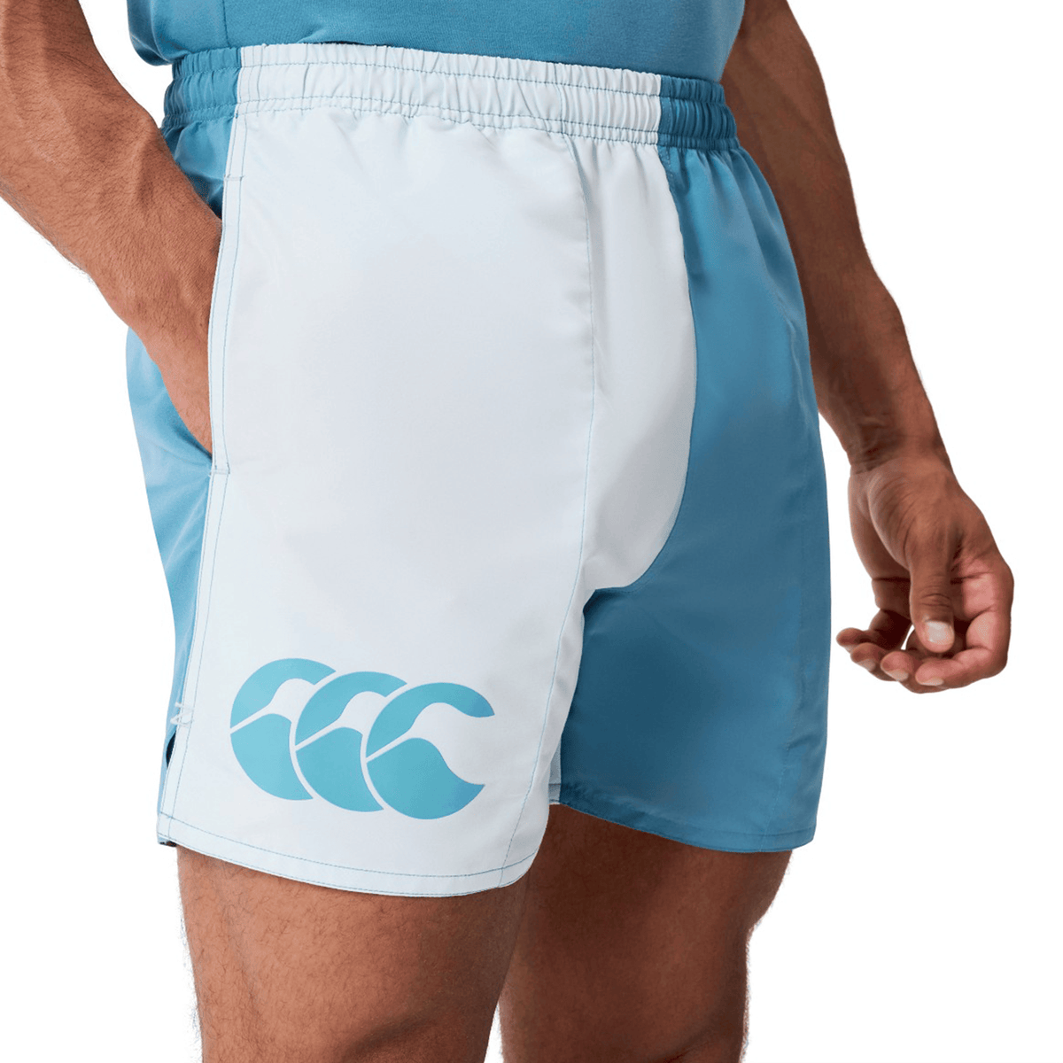 A person wears Canterbury Fundamental Harletic 3″ Rugby Shorts in light blue and white, featuring the wave logo on the left leg.