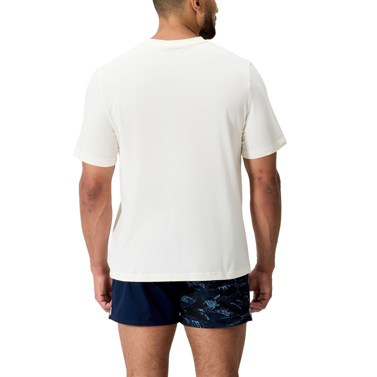 A man stands facing away, wearing a plain white Force CCC T-Shirt by Canterbury and navy blue patterned shorts, against a white background.