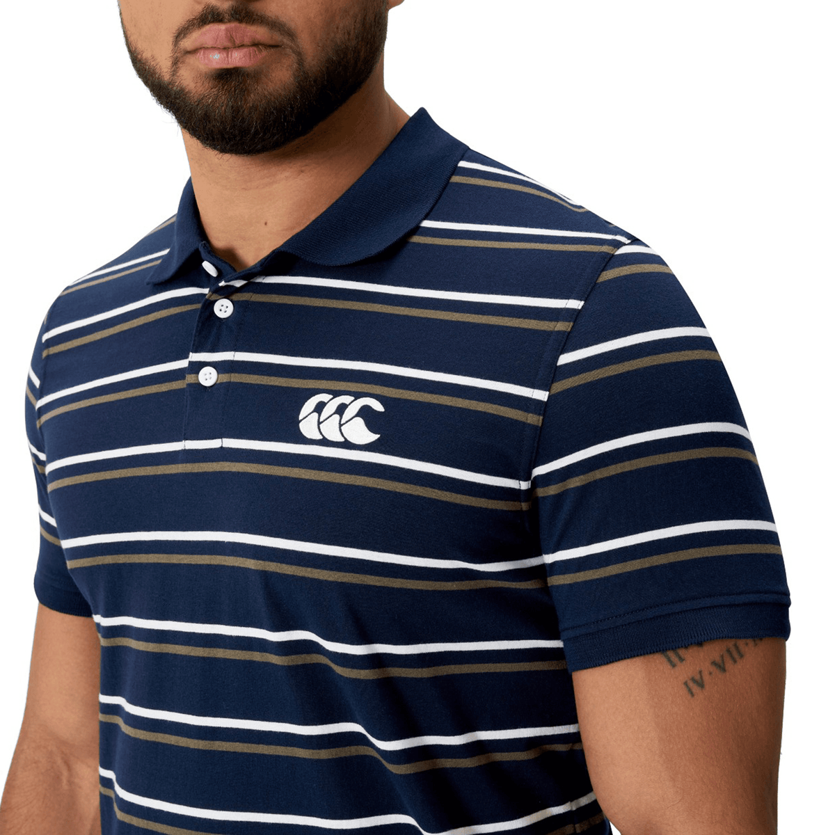 A man is wearing the Canterbury Yarn Dye Stripe Polo by Canterbury, featuring a navy blue base with horizontal white and brown stripes and a white logo on the chest.
