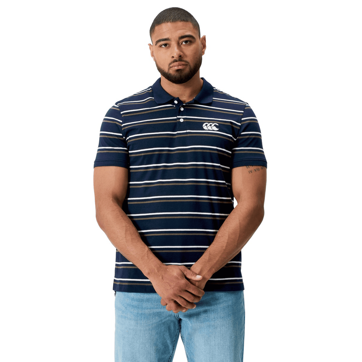 A man wearing the Canterbury Yarn Dye Stripe Polo by Canterbury in navy blue and white, paired with light blue jeans, stands against a white background with his hands clasped.