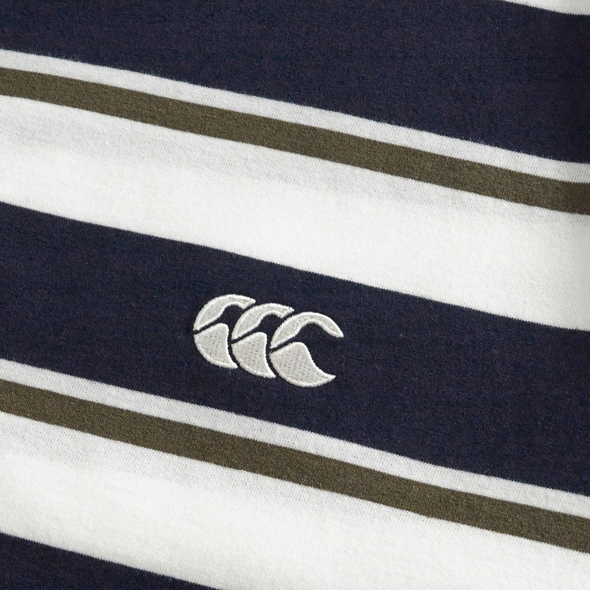 Close-up of the Fundamental Yarn Dye Stripe T-Shirt by Canterbury, featuring navy, white, and olive green stripes with the Canterbury (CCC) logo embroidered in white.