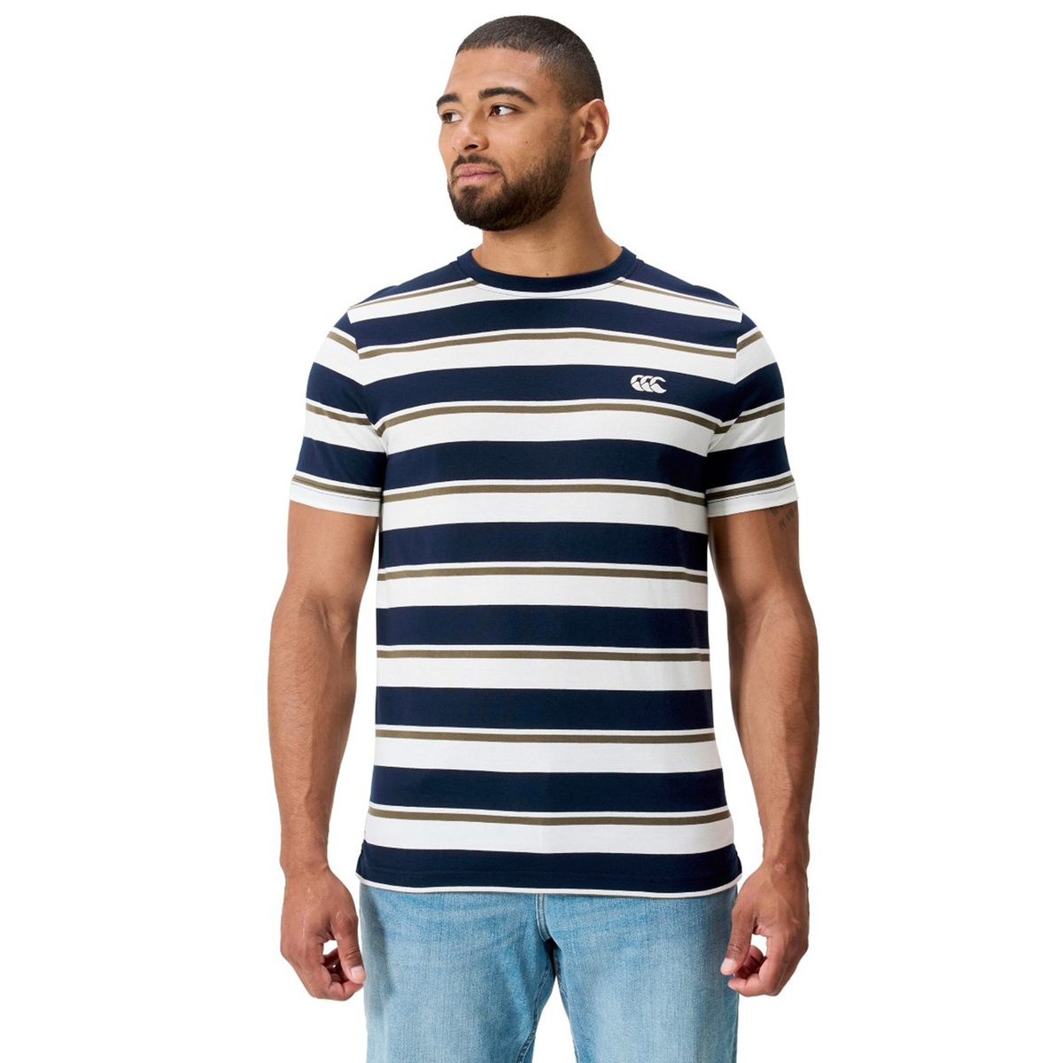 A man in the Canterbury Fundamental Yarn Dye Stripe T-Shirt and light blue jeans stands slightly left against a white background, channeling a subtle Canterbury rugby-inspired style.