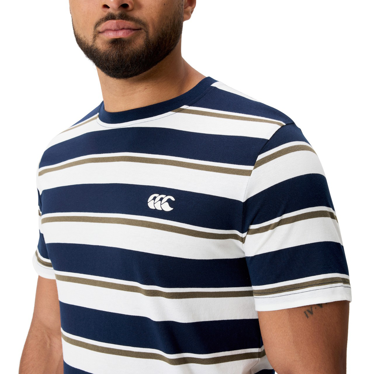 A man stands against a plain background wearing the Canterbury Fundamental Yarn Dye Stripe T-Shirt in navy, white, and olive green, featuring a small white chest logo and showcasing its rugby-inspired style.