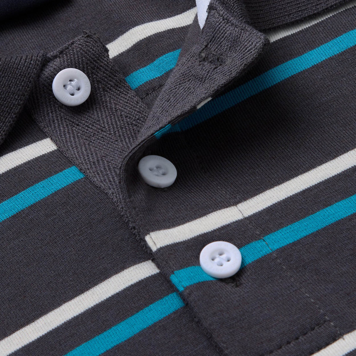 Close-up of the Canterbury Yarn Dye Stripe Polo, featuring gray fabric with white, blue, and beige horizontal stripes and white buttons along the placket—a fresh update on the classic Canterbury rugby polo style.