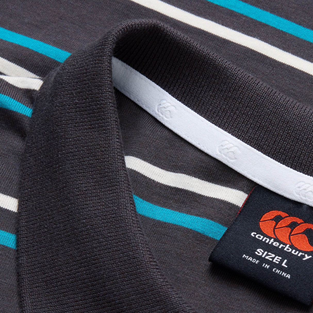 Close-up of the Canterbury Yarn Dye Stripe Polo, a rugby-style shirt by Canterbury featuring blue, white, and gray stripes, with a detailed view of the collar and a label showing size L and made in China.