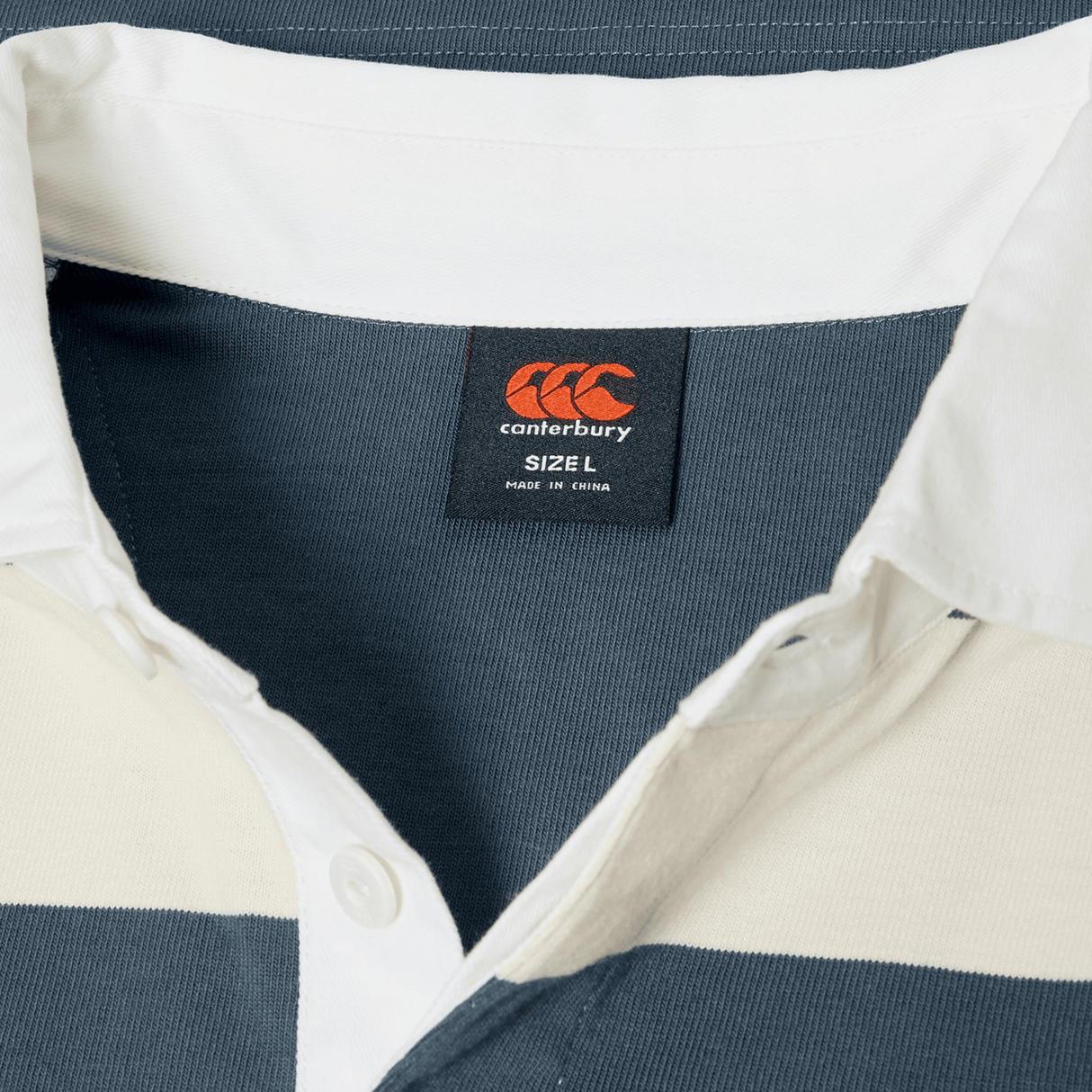 Close-up of the Canterbury Yarn Stripe Rugby Jersey by Canterbury, featuring navy and white yarn-dye stripes, collar, buttons, and a size L label.