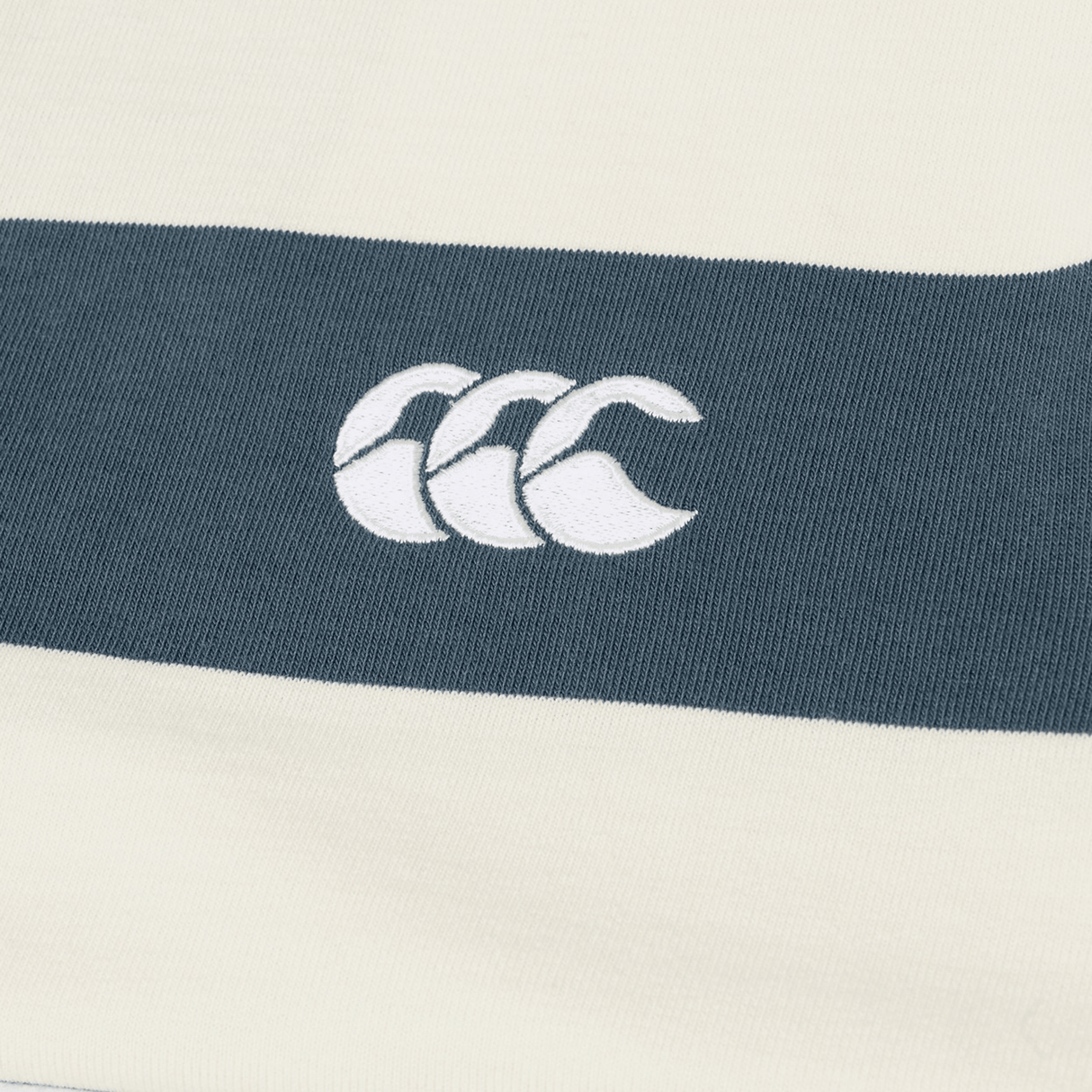 Close-up of the Canterbury Yarn Stripe Rugby Jersey by Canterbury, featuring cream and dark gray yarn-dyed stripes and an embroidered white logo.