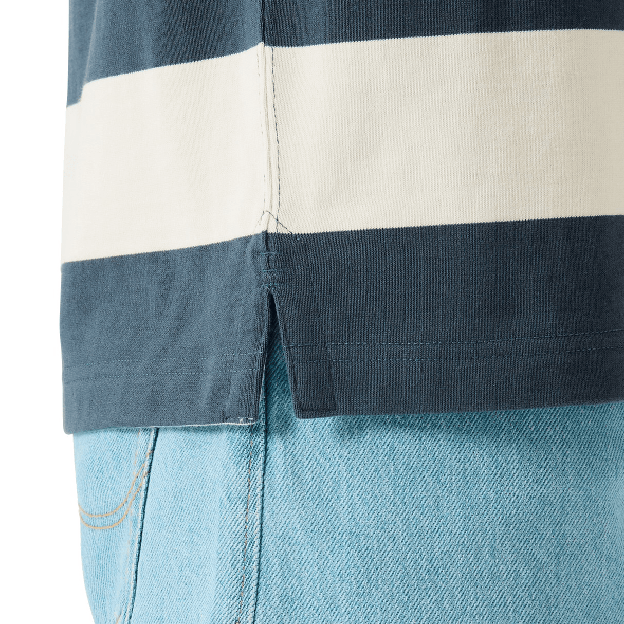 Close-up of a person wearing light blue jeans and the Canterbury Yarn Stripe Rugby Jersey by Canterbury, featuring navy and white stripes and a side slit at the hem.
