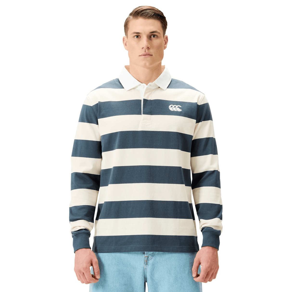 A man in a Canterbury Yarn Stripe Rugby Jersey and light blue jeans stands facing forward against a white background.