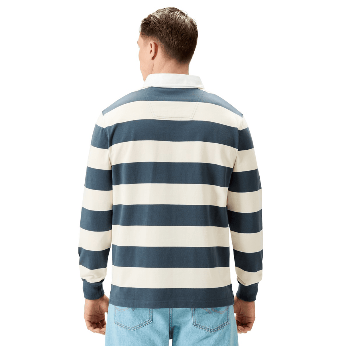 Someone wearing the Canterbury Yarn Stripe Rugby Jersey by Canterbury, featuring blue and white yarn-dye stripes and long sleeves, paired with light blue jeans, is shown from the back.