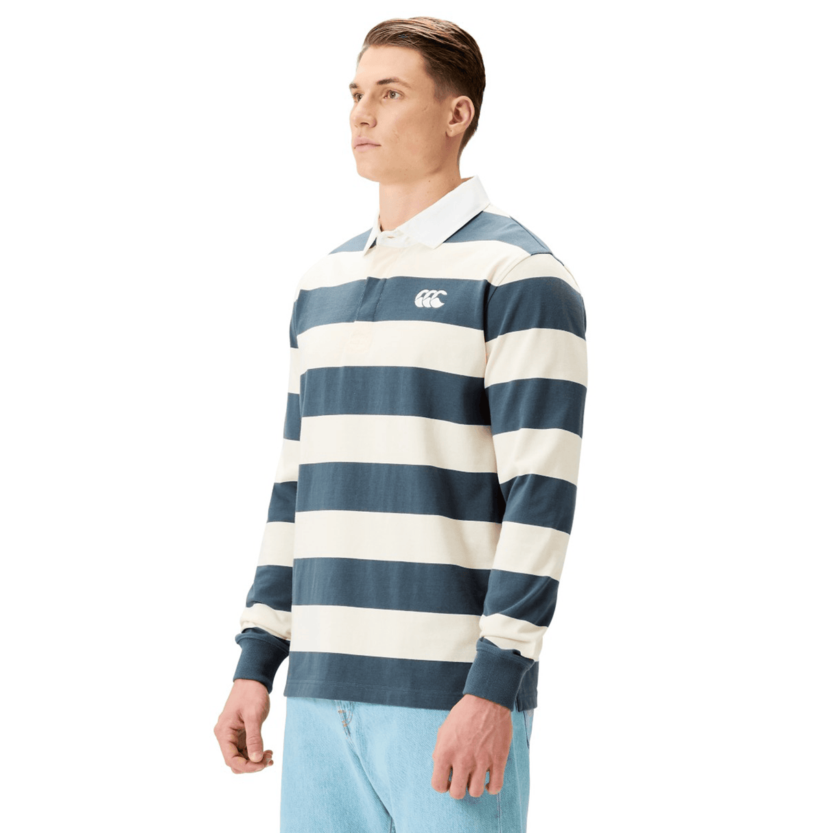 A person wearing the Canterbury Yarn Stripe Rugby Jersey by Canterbury and light blue jeans stands against a plain background.
