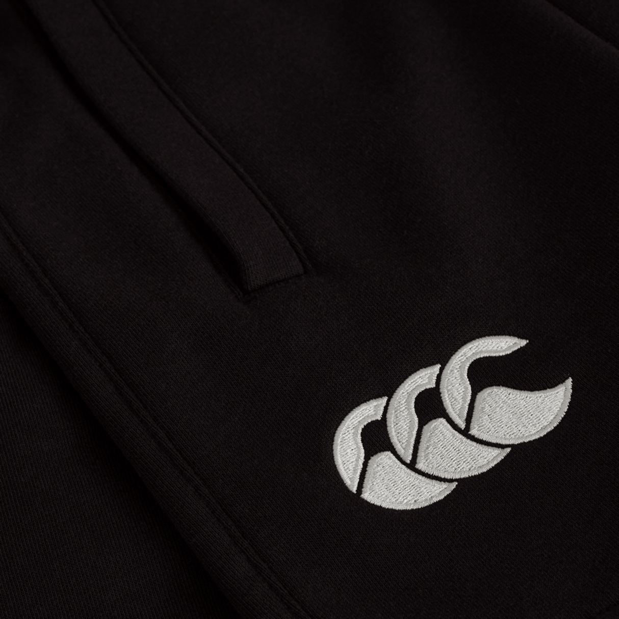 Close-up of the Women's Ireland 25/26 Knit Short by Canterbury, showing a white embroidered triple-shape logo on black fabric. Perfect addition to women's sports shorts collections.