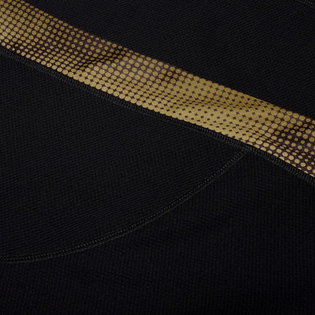 Close-up of the black textured fabric from the Canterbury Tempo+ Drill Top, featuring a diagonal strip with a gold and brown dotted pattern.