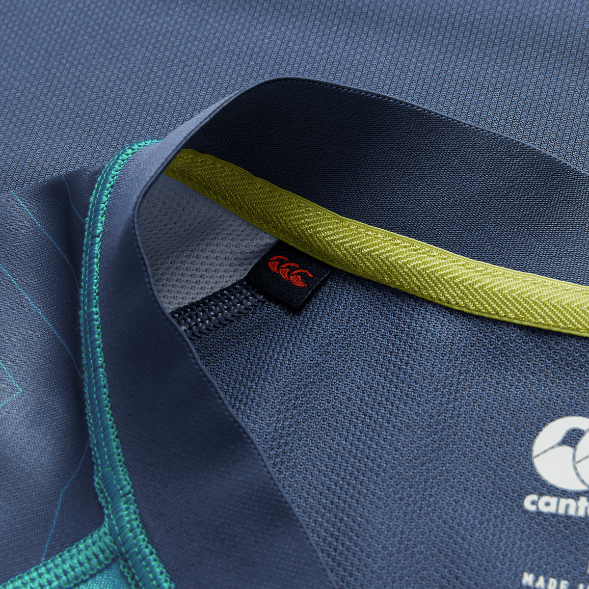Close-up of the Ireland 26/27 Summer Tour Training Pro Jersey by Canterbury, showcasing a blue design, yellow inner collar, black and red tag, teal stitching, and the Canterbury logo in Pro Fit style.
