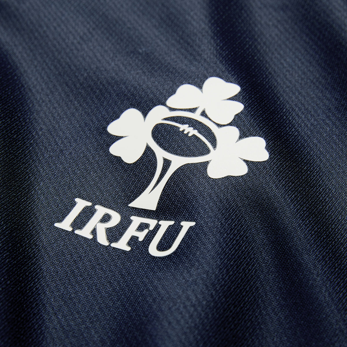 The Ireland 26 Training Pro Jersey by Canterbury features the IRFU logo—a shamrock and rugby ball design—printed in white on dark blue textured fabric, and incorporates Canterbury’s signature VapoDri technology for optimal comfort.