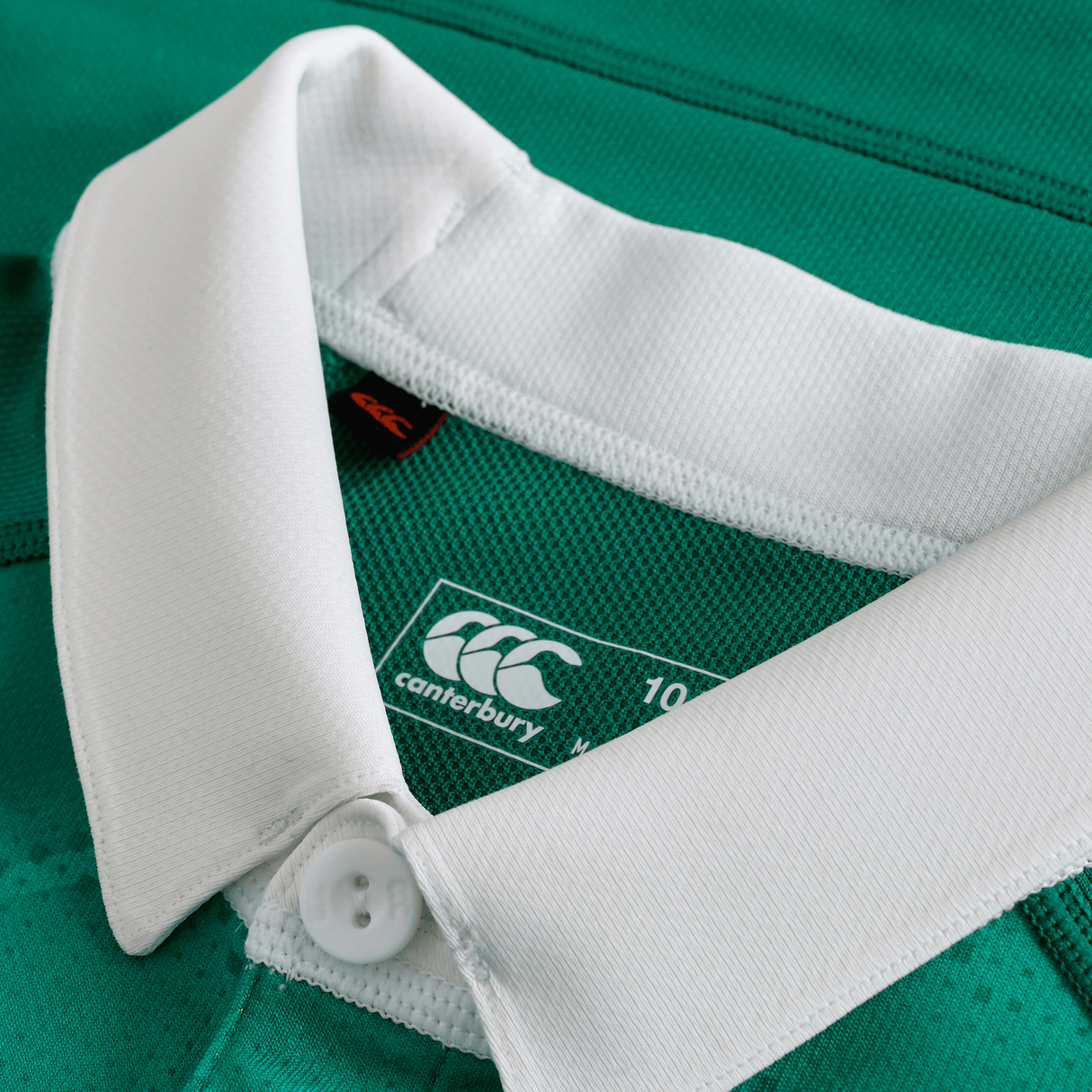 Close-up of the Canterbury Youth Ireland 25/26 Home Pro Jersey in green, featuring a white collar with button, visible brand logo, and size label.