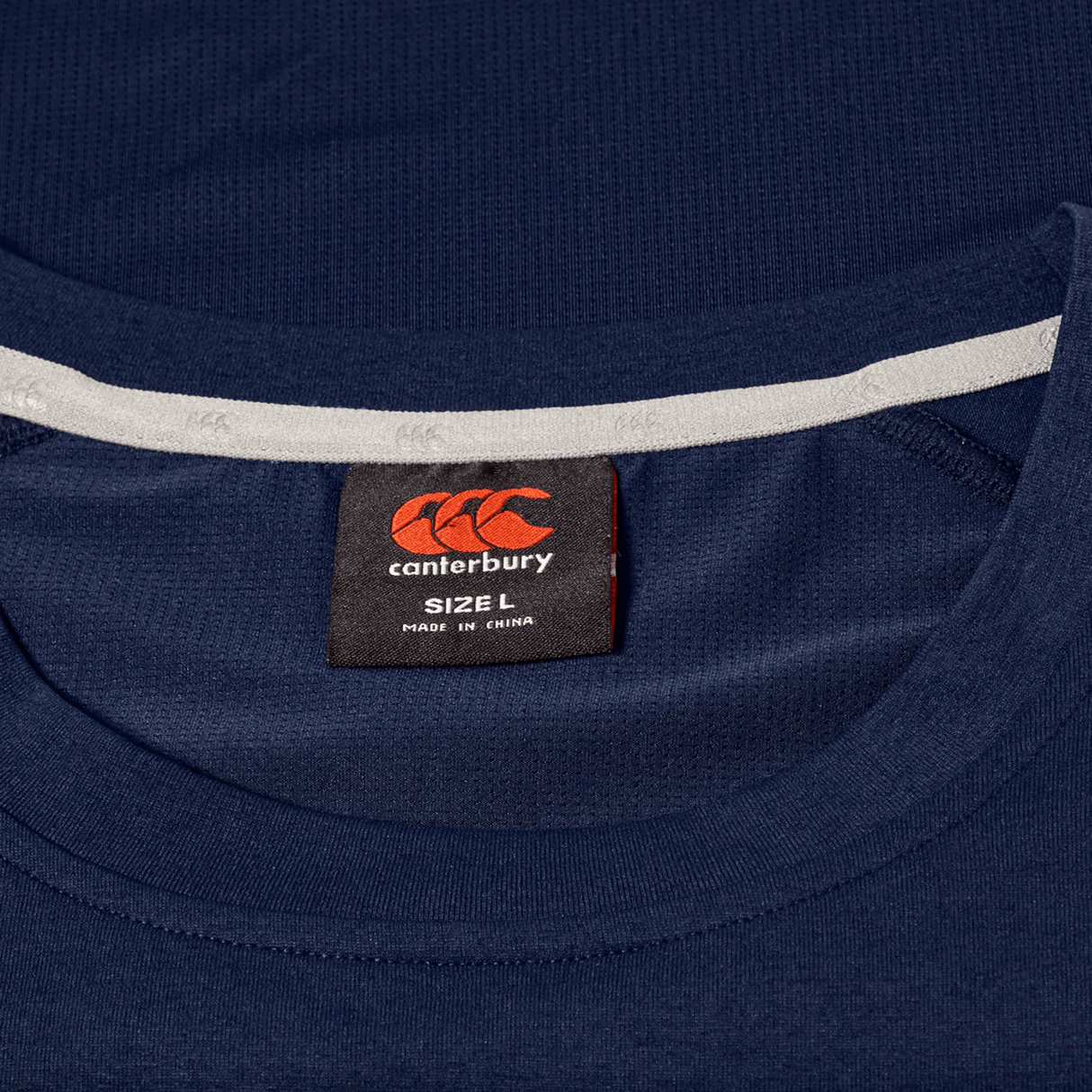 Close-up of a Canterbury Everest Dart Tech T-Shirt in navy blue, showing the inside neck label with the Canterbury logo, size L, and "Made in China" text.