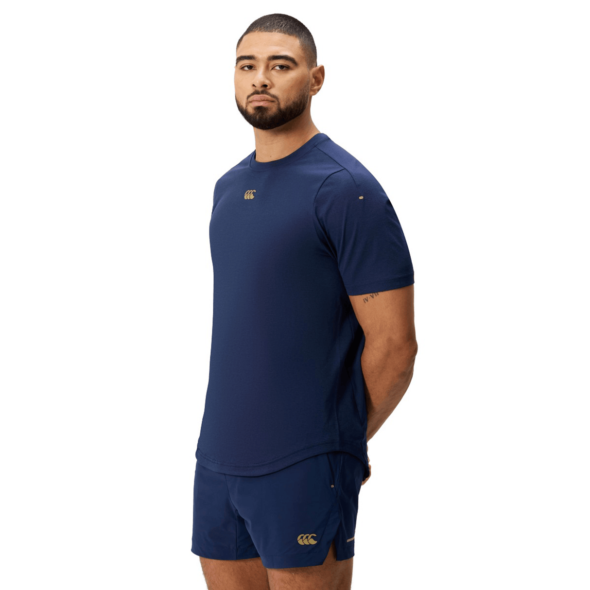 Man wearing the Canterbury Everest Dart Tech T-Shirt by Canterbury in navy blue with matching shorts, standing against a white background with his arms behind his back.