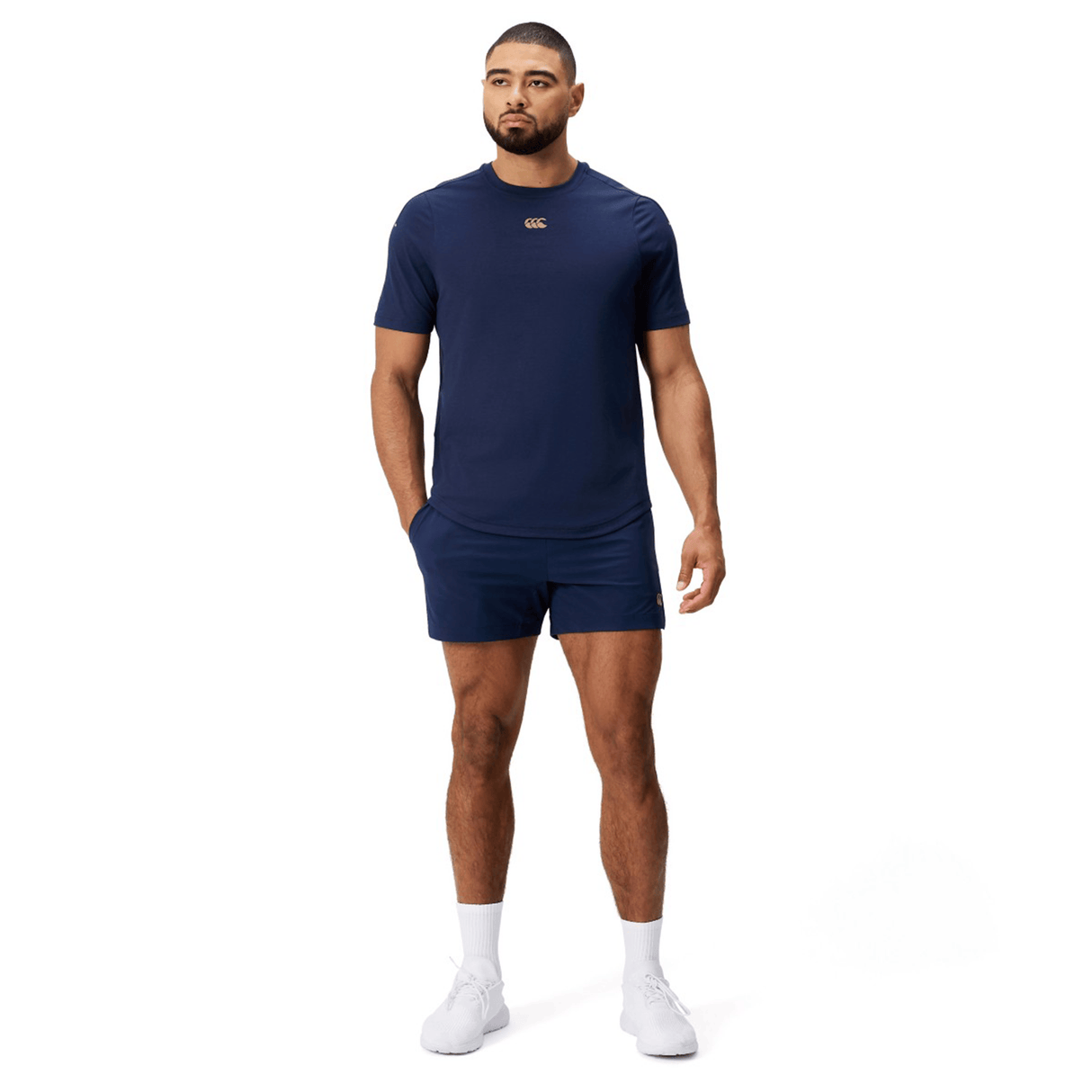 A man faces forward wearing the Canterbury Everest Dart Tech T-Shirt in navy blue, matching shorts, and white sneakers against a plain white background.