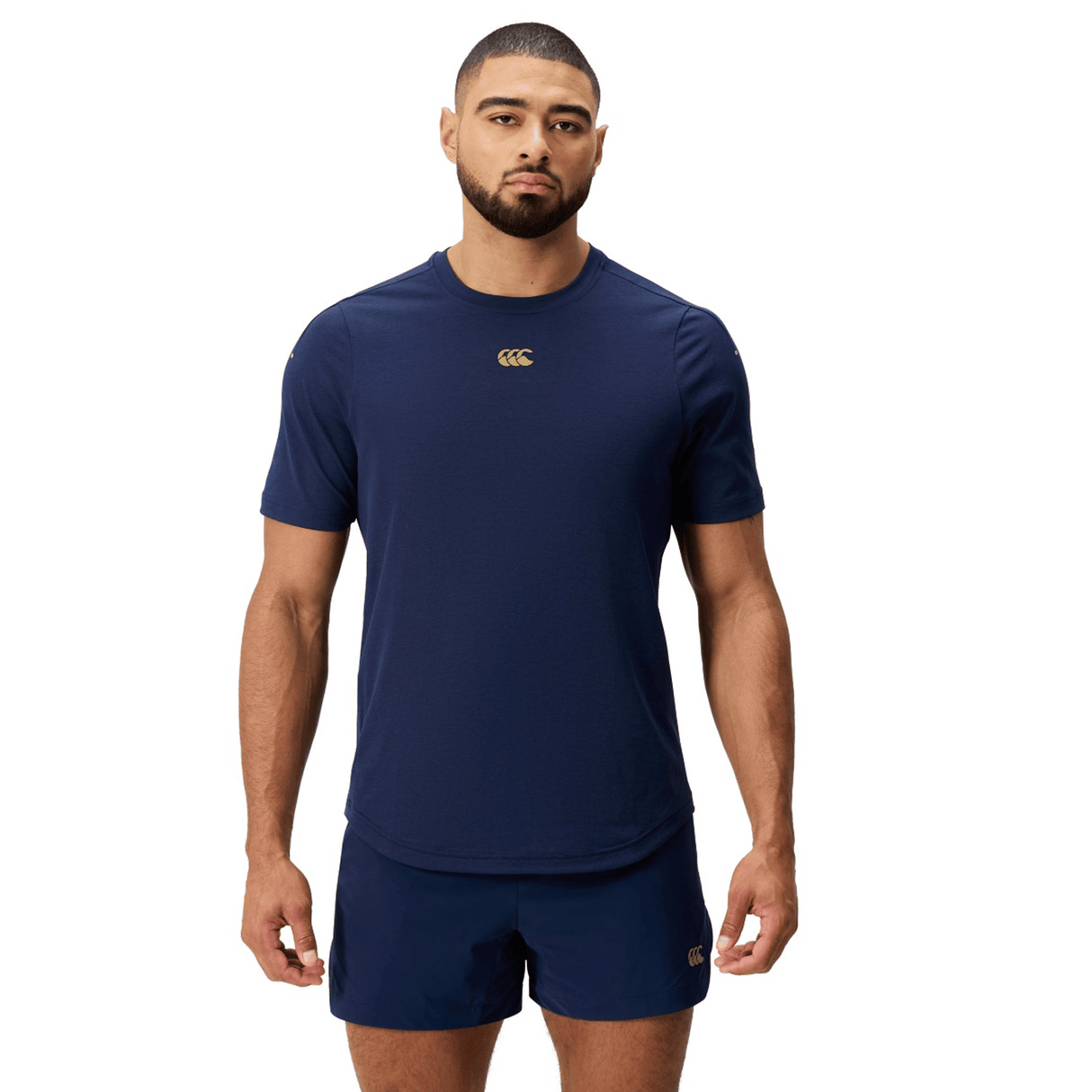 A man wearing a Canterbury Everest Dart Tech T-Shirt in navy blue polyester and matching shorts stands facing forward against a white background.