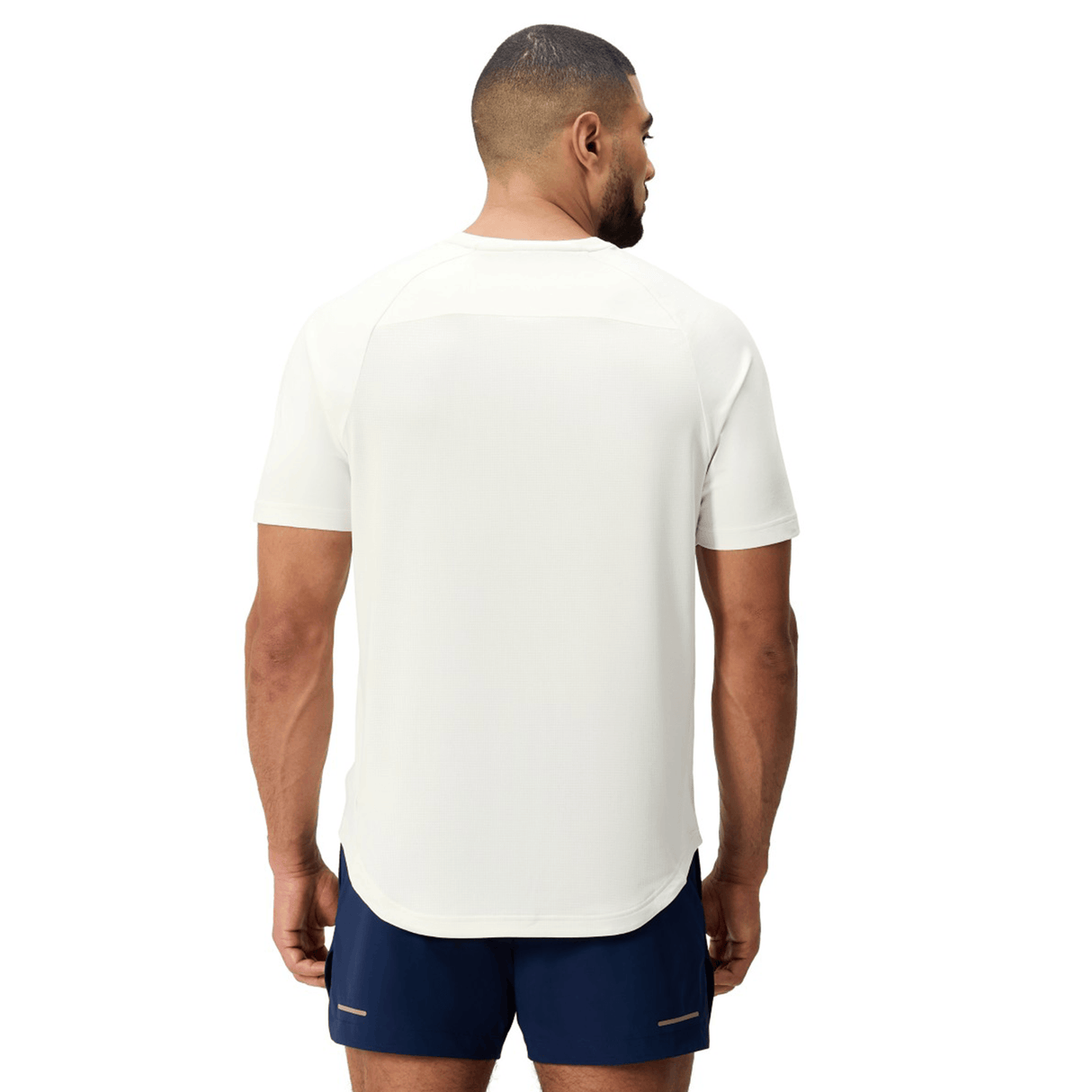 A man stands facing away, wearing a Canterbury Everest Dart Tech T-Shirt and navy athletic shorts against a plain background.