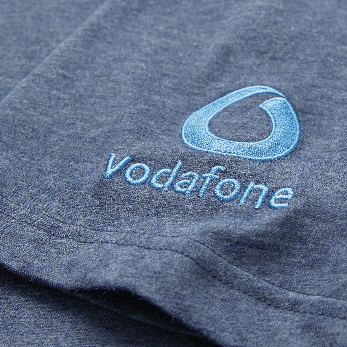 A close-up of the Ireland 26/27 Summer Tour Team Cotton T-Shirt by Canterbury in blue, featuring an embroidered Vodafone logo and light blue text—ideal for fans supporting the summer tour.
