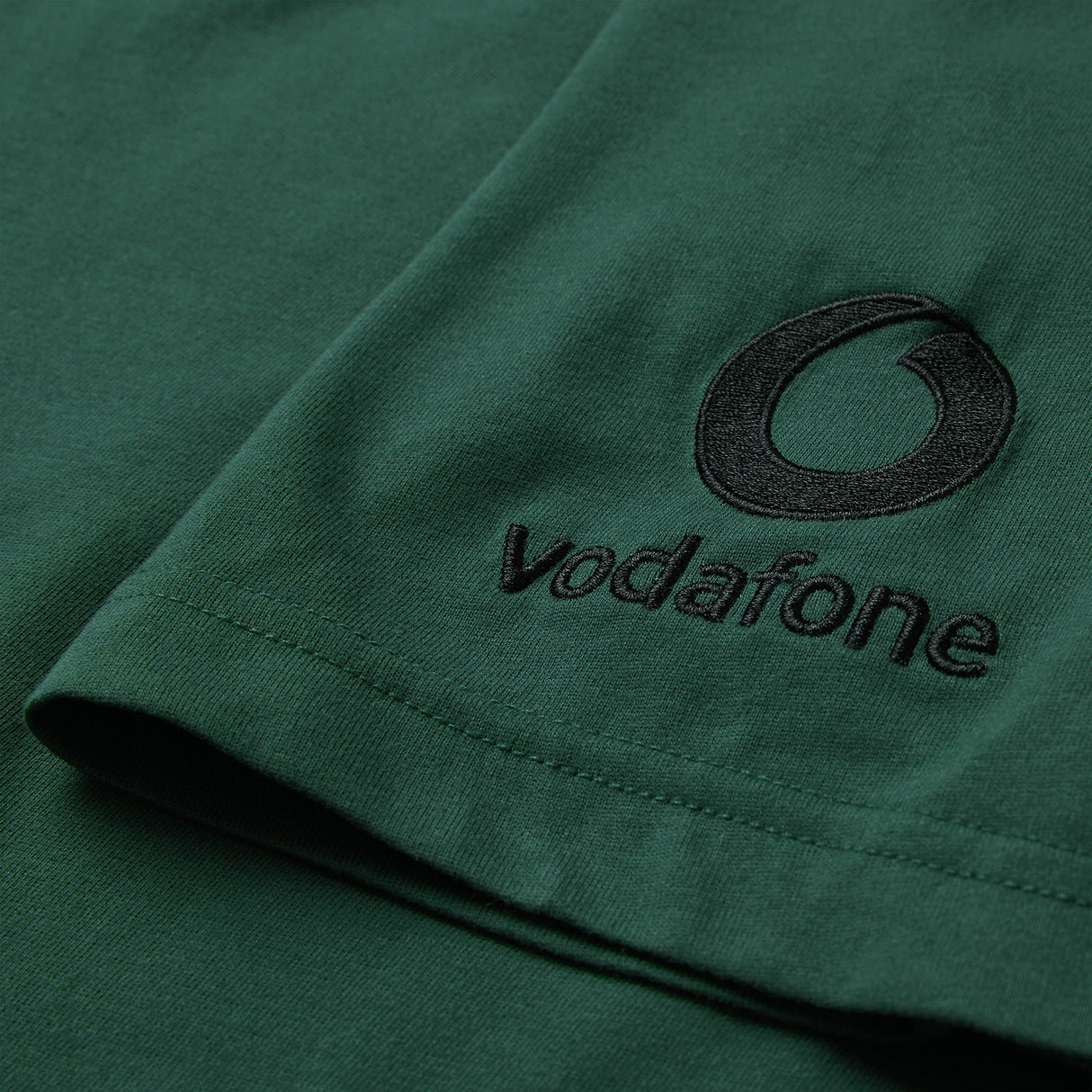 Close-up of the green fabric from the Ireland 26 Team Cotton T-shirt by Canterbury, featuring the Vodafone logo and name embroidered in black on the sleeve.