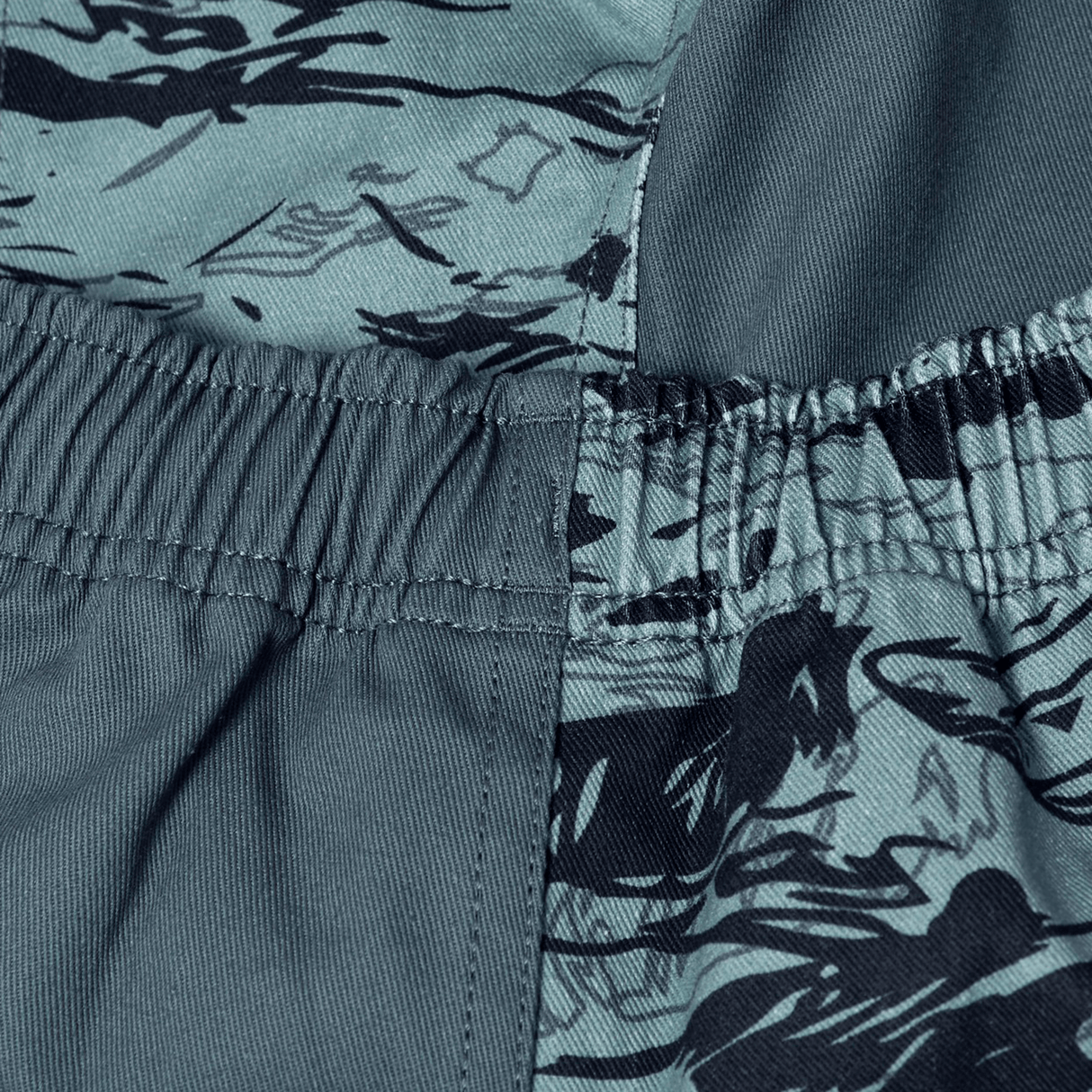 Close-up of blue-green fabric with a black abstract pattern and elastic waistband seam, highlighting the durable design of Canterbury’s Force Harlequin Drill Short.