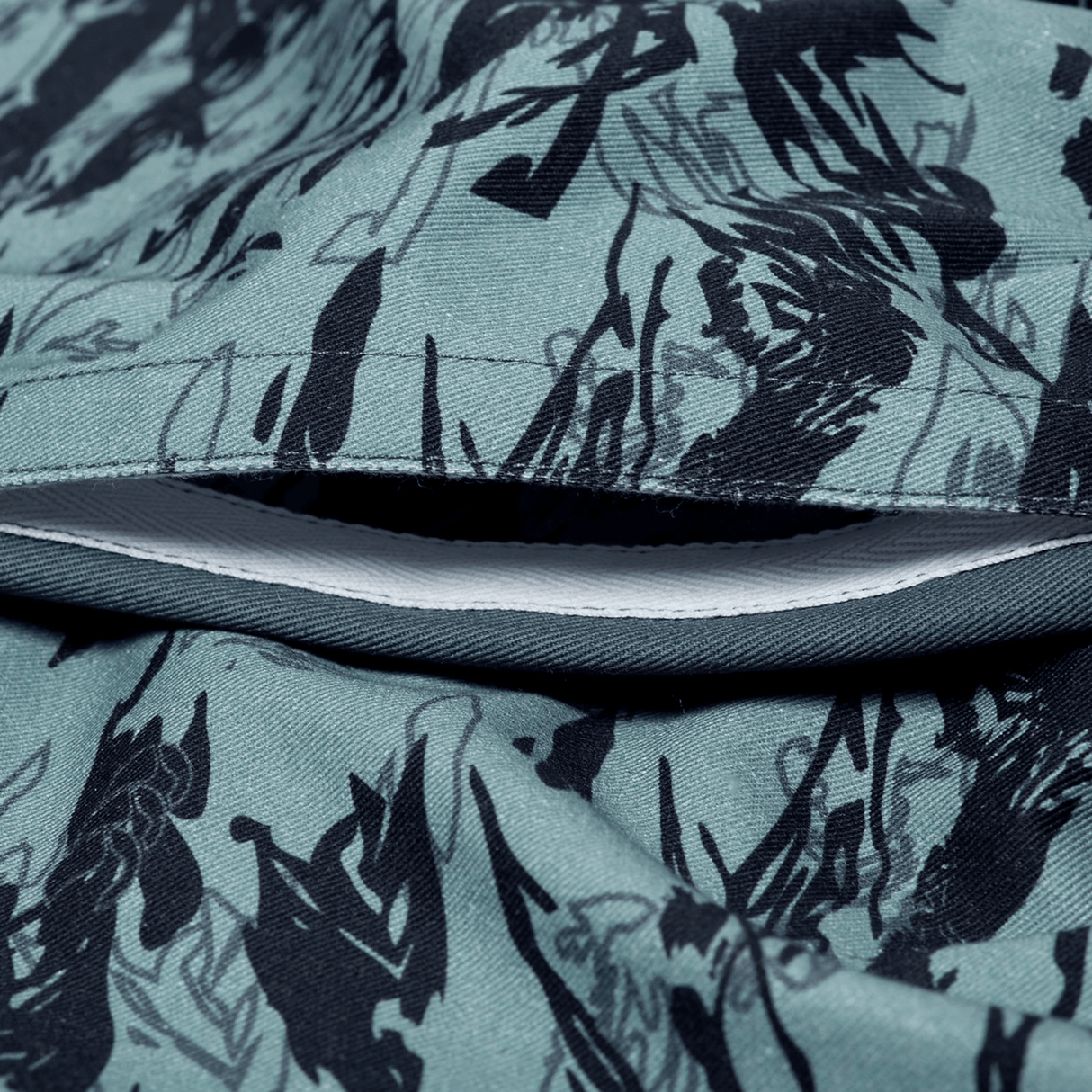 Close-up of an unzipped pocket on the Canterbury Force Harlequin Drill Short by Canterbury, crafted from green fabric with a striking black abstract pattern.