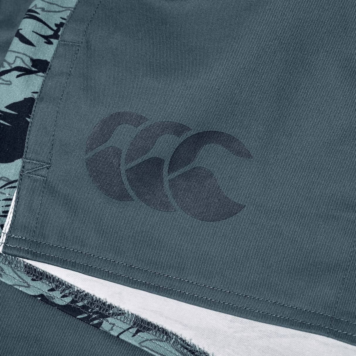 Close-up of Canterbury Force Harlequin Drill Short in teal, featuring the Canterbury logo and a patterned seam trim, blending military-inspired utility with durable performance for training.