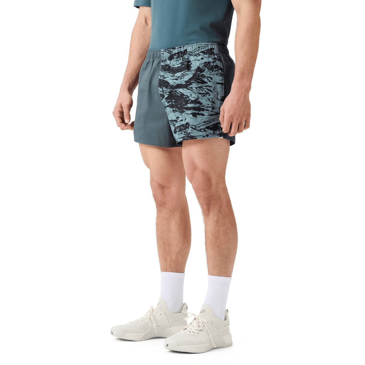 Man in a teal athletic shirt, Canterbury Force Harlequin Drill Shorts by Canterbury, white crew socks, and white sneakers stands against a plain white background.