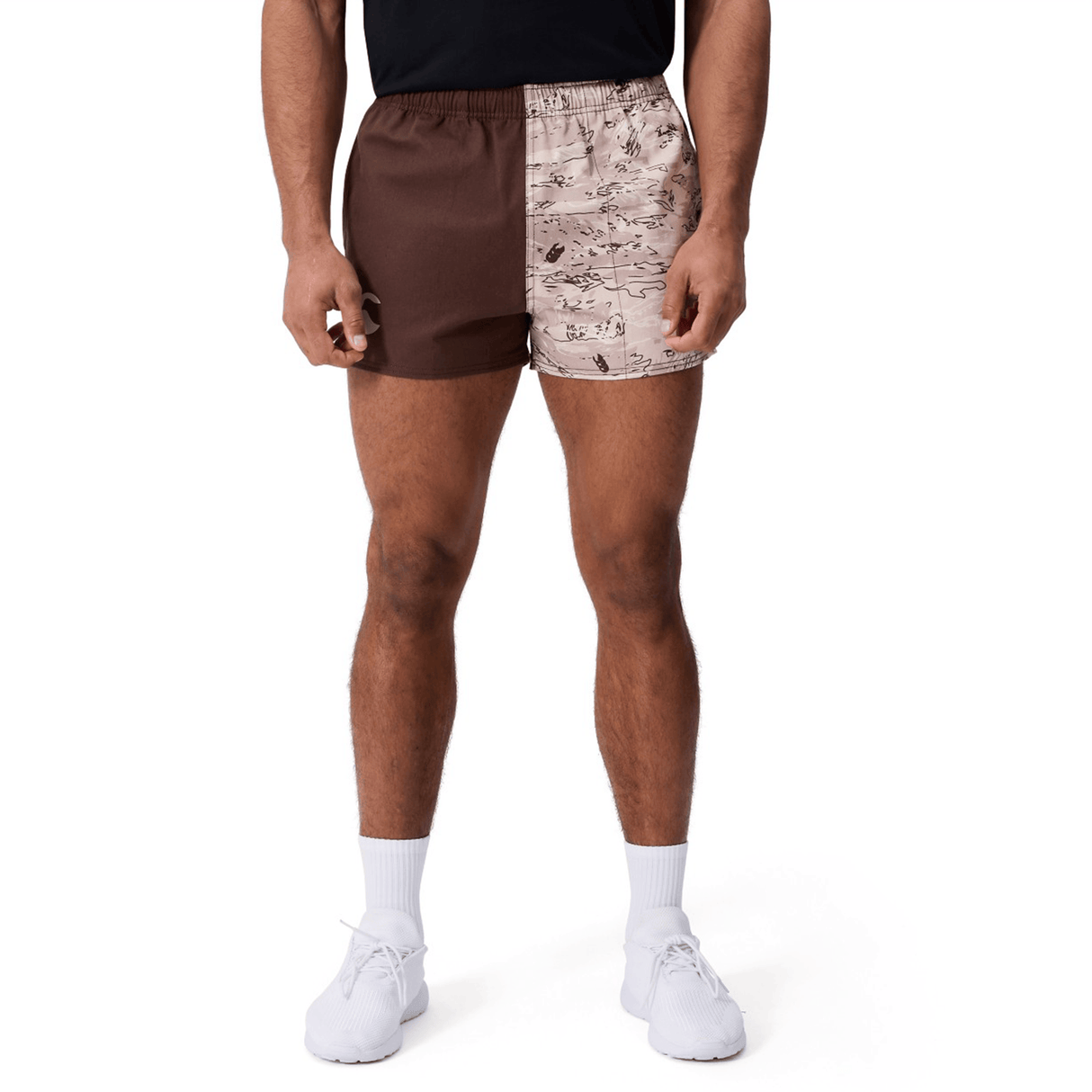 A person wearing Canterbury Force Harlequin Drill Shorts by Canterbury—featuring one brown leg and one patterned beige leg—paired with a black shirt, white socks, and white sneakers.