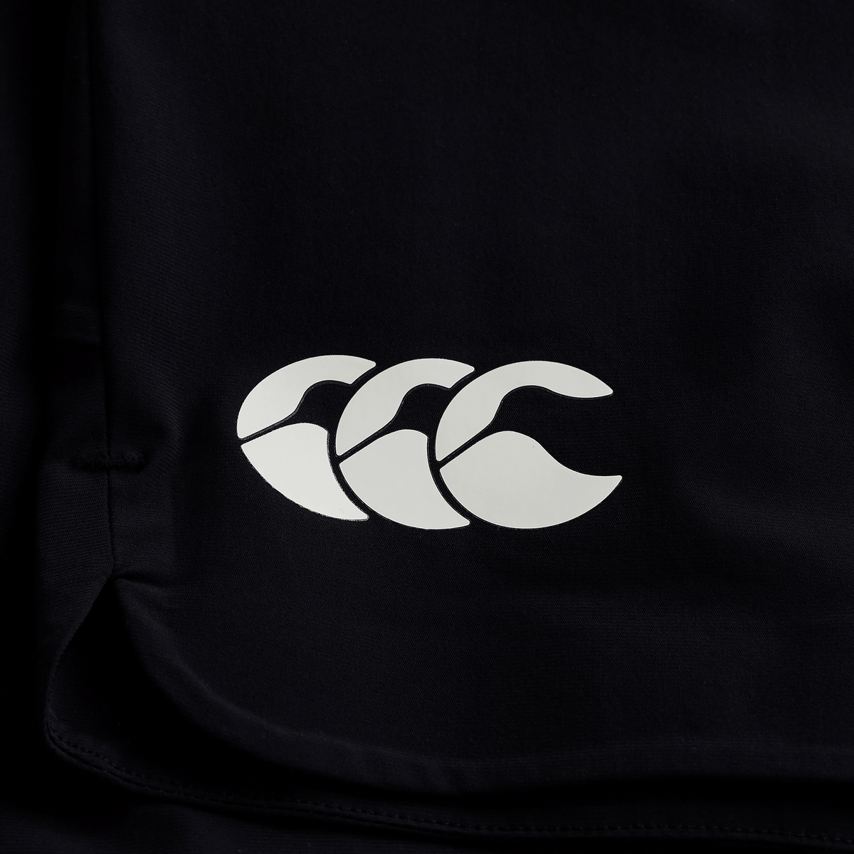 Close-up of black fabric with a white Canterbury logo—three overlapping C’s—featured on the official Ireland 25/26 Gym Training Short by Canterbury.