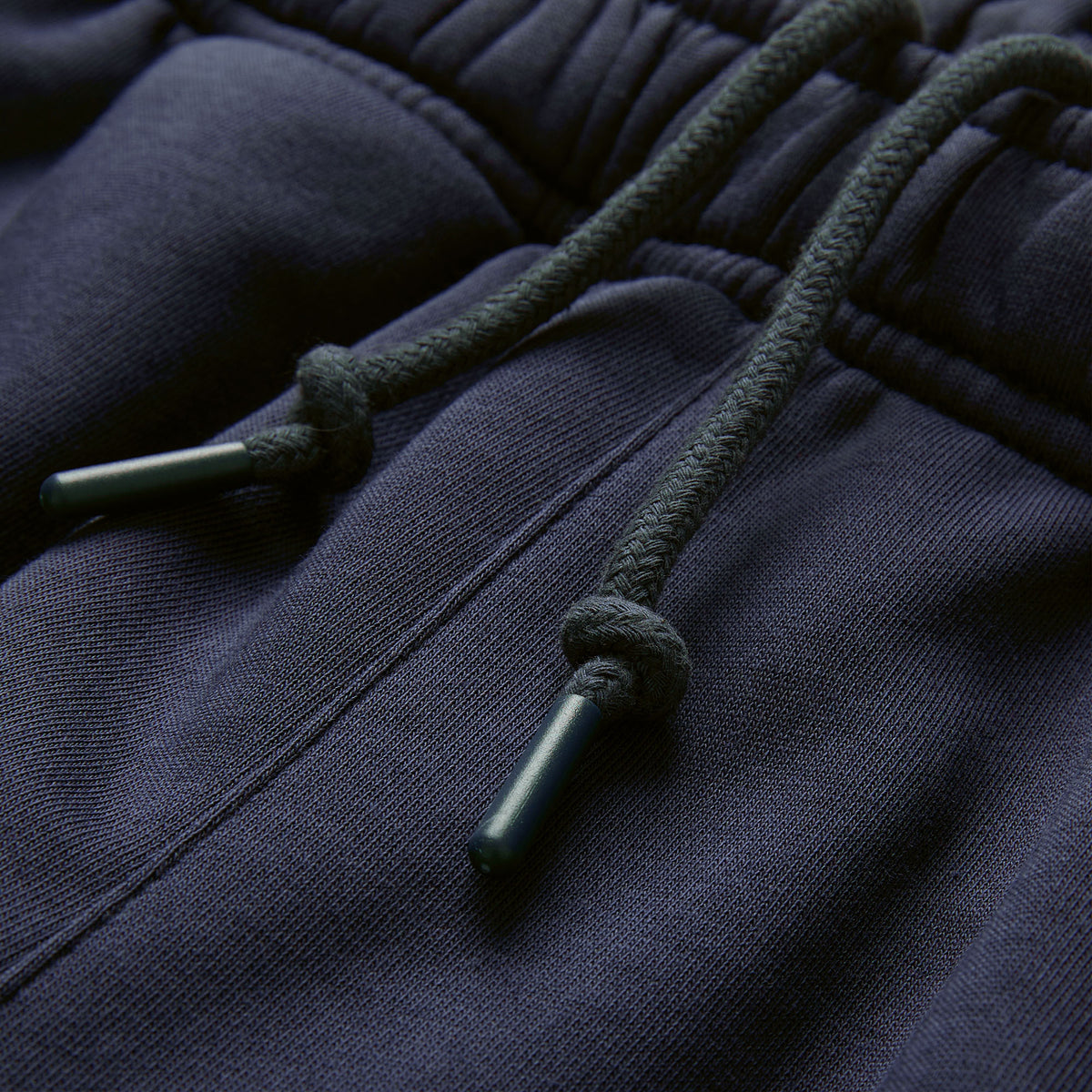 Close-up of dark blue sweatpants featuring an elastic waistband with two drawstrings tied in knots and plastic aglets, reminiscent of the secure fit found in the Canterbury Ireland 26 Legends 7″ Shorts.