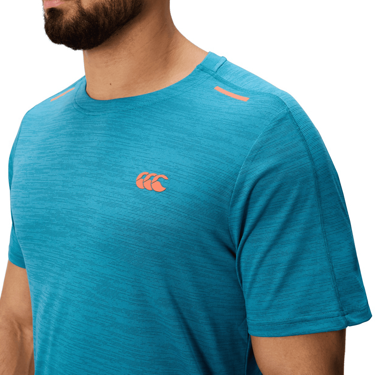 A person wearing a blue Canterbury Tempo Relaxed T-Shirt with breathable fabric, orange Canterbury logo on the chest, and orange details near the shoulders.