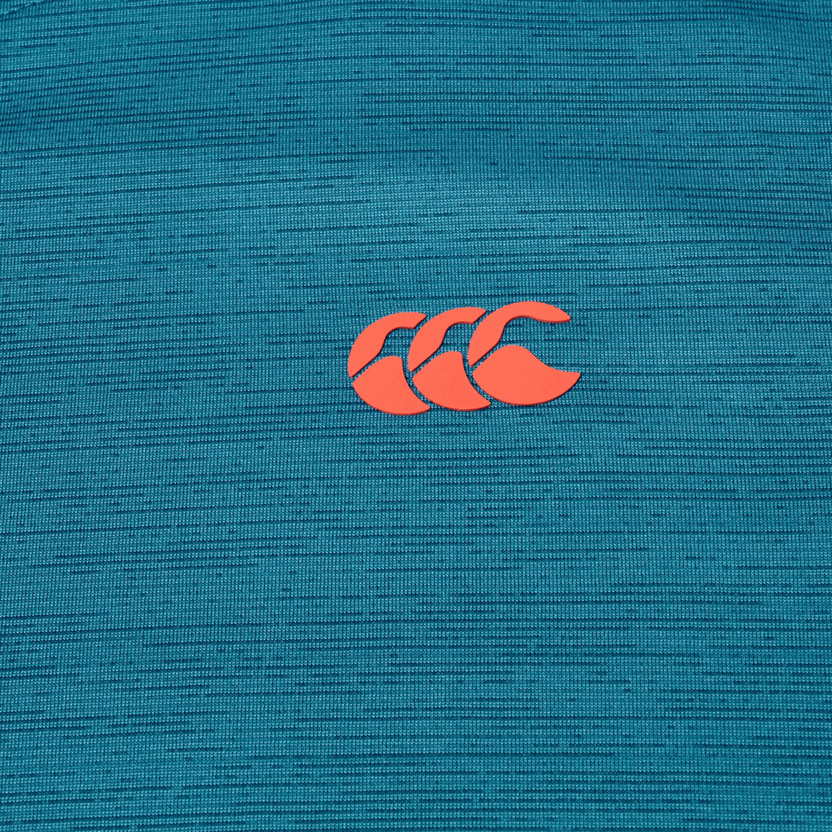 Close-up of the Canterbury Tempo Relaxed T-Shirt by Canterbury, shown in teal breathable fabric with a red "CCC" logo of three overlapping C shapes at the center.