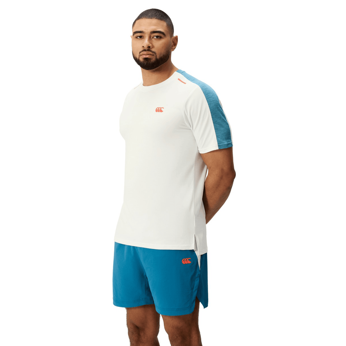 A man wears a white Canterbury Tempo Relaxed T-Shirt with teal shoulder panels and matching Canterbury shorts, set against a white background.