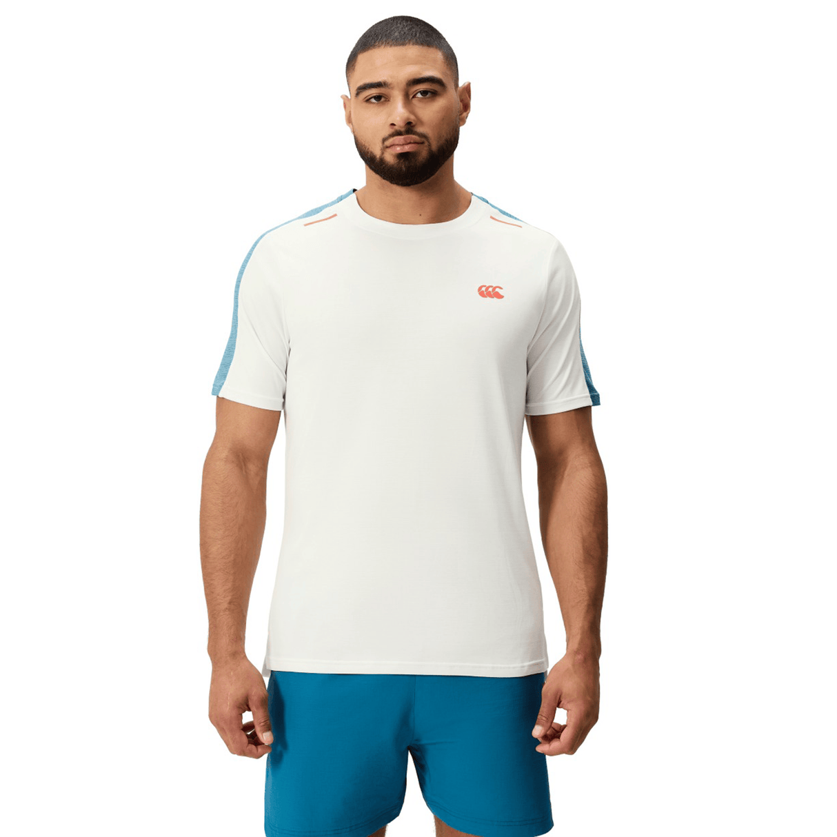 A man stands facing forward against a white background wearing the Canterbury Canterbury Tempo Relaxed T-Shirt, made from breathable fabric, paired with blue shorts.