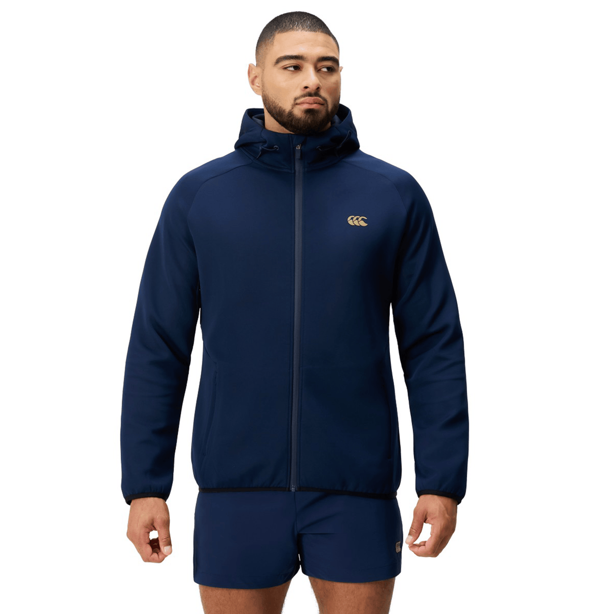 A man wearing a Canterbury Everest Full Zip Hoodie and matching navy shorts stands facing forward against a white background.