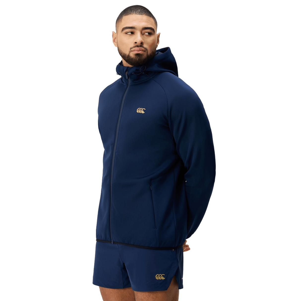 Man in a navy Canterbury Everest Full Zip Hoodie and matching shorts with gold Canterbury logos, standing against a plain white background.