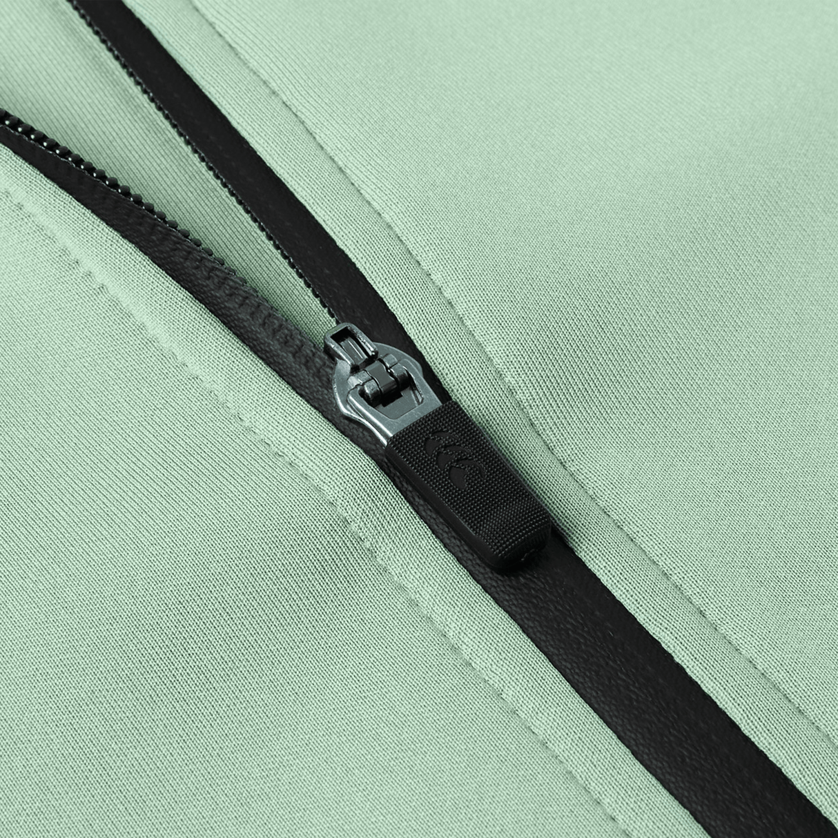 Close-up of a black zipper on light green fabric, partially unzipped, displaying detailed stitching and texture typical of the Canterbury Everest Zip Thru Hoodie by Canterbury.
